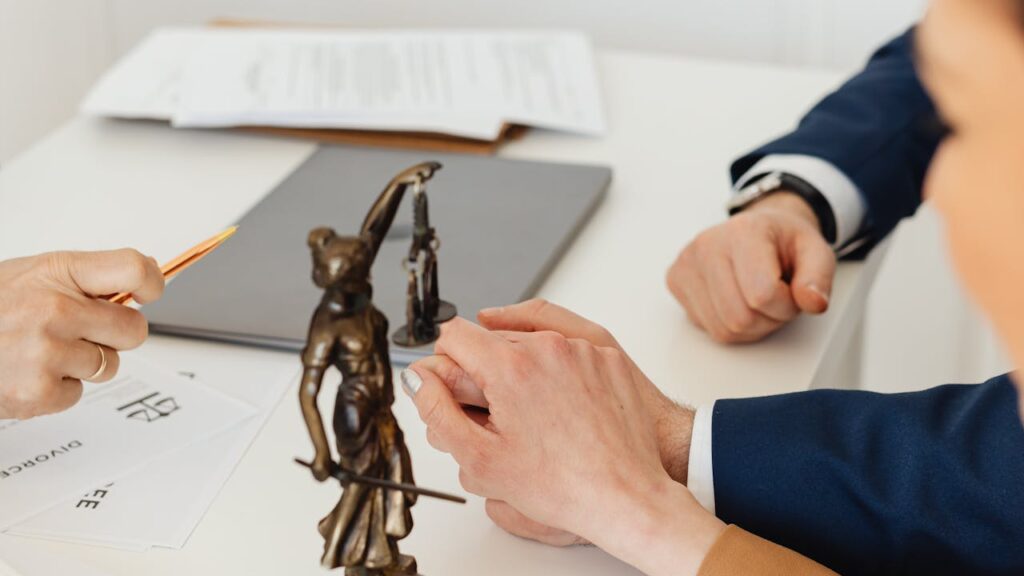 法務の資料と天秤の置物を前に話し合う人の手元